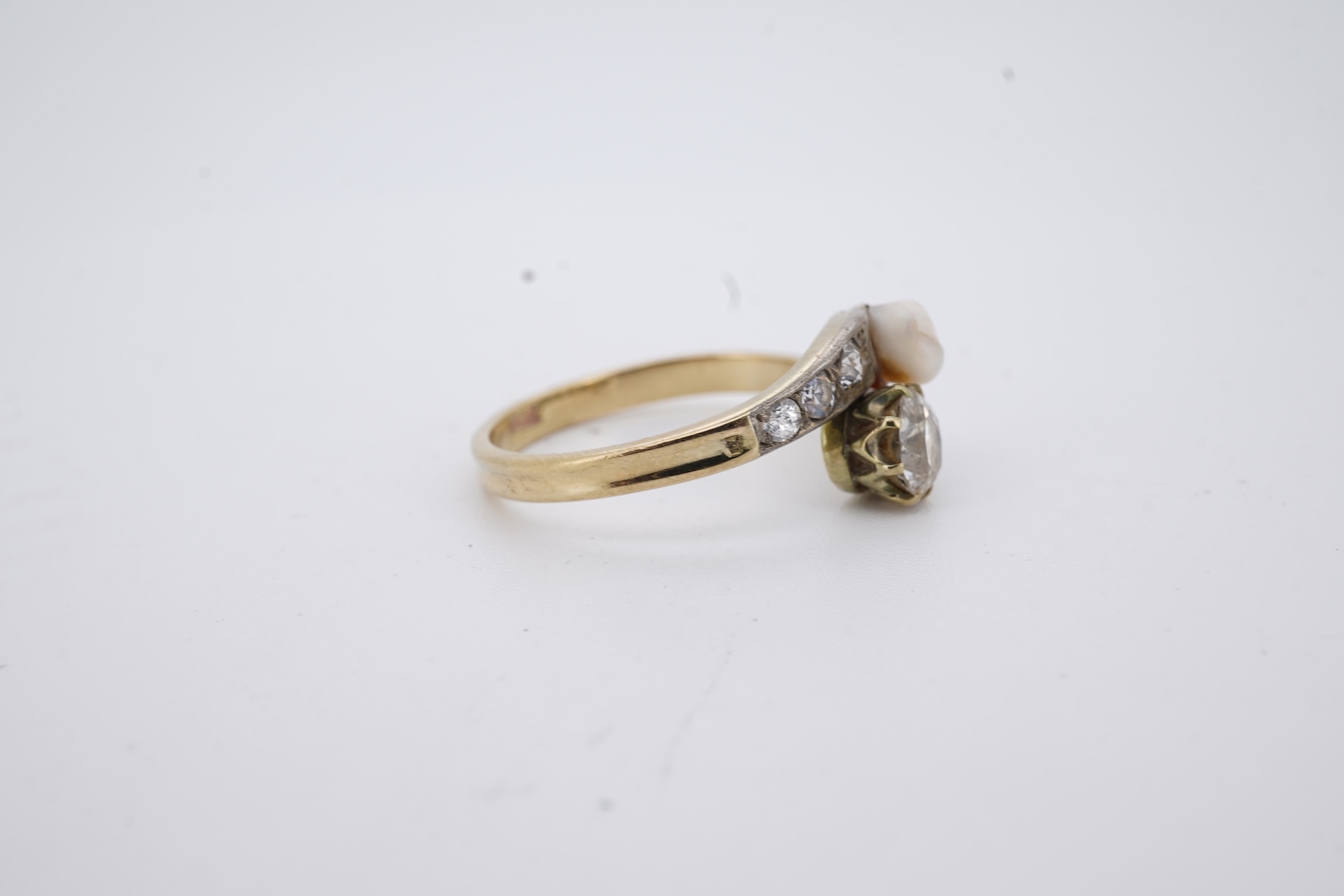 A yellow meta (stamped 18ct) cultured pearl and diamond set crossover ring, with six stone graduated diamond set shoulders, size M, gross weight 2.6 grams (pearl nacre a.f.).